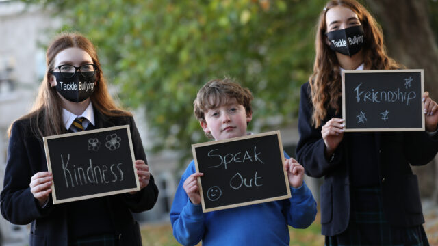 This is a photo of three students smiling and holding signs that say "Firendship", "Kindness", and "Speak Out".