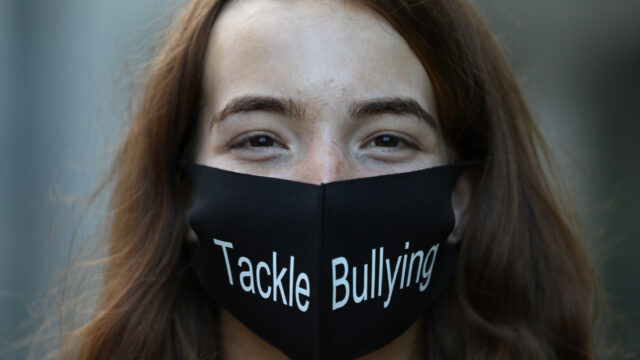 This is a photo of a girl looking at the camera. She is wearing a mask that has the words Tackle Bullying on it.