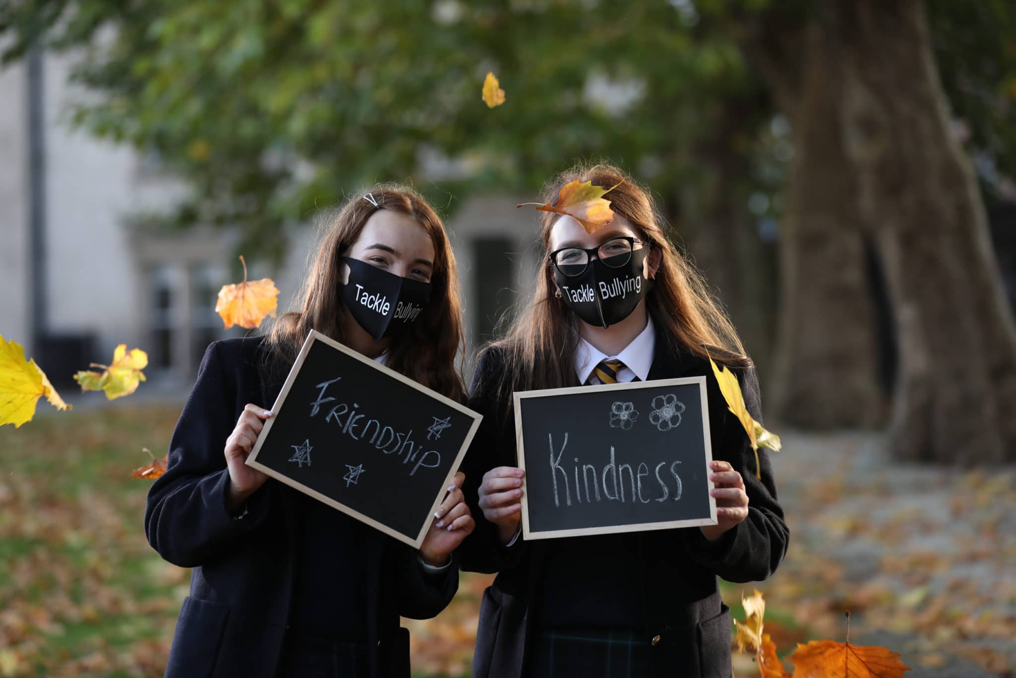 This is a photo of two students smiling and holding signs that say "Friendship" and "Kindness". They are both wearing masks that say "Tackle Bullying" on them.