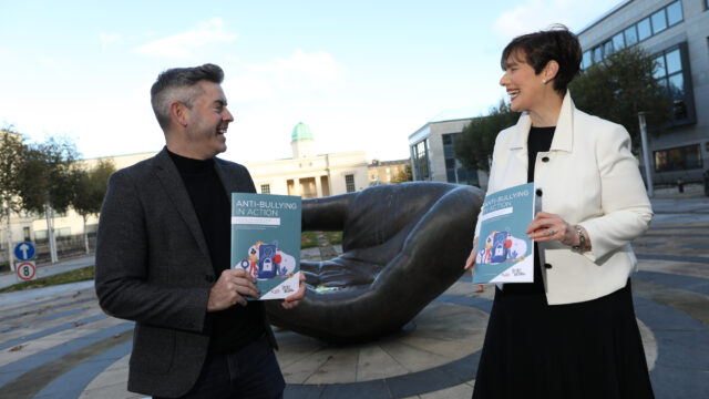 This is a photo of Darran Heaney and Norma Foley TD talking and laughing. Both are hold a booklet titled "Anti-Bullying in Action".