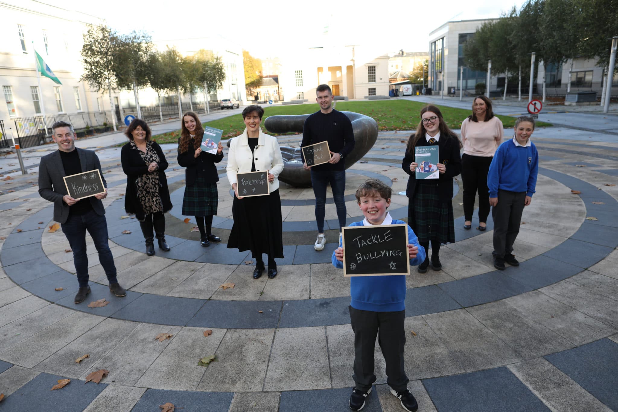 This is a photo of a group of poeple, adults and children. They are holding signs with positive messages on them along with booklets titled "Anti-Bullying in Action".